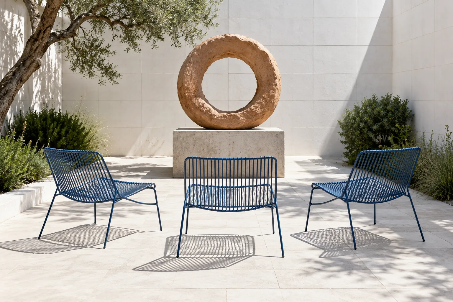 Illustration: Wide view of three blue wire chairs facing an original unglazed clay ring sculpture on a concrete plinth in a white tiled courtyard.