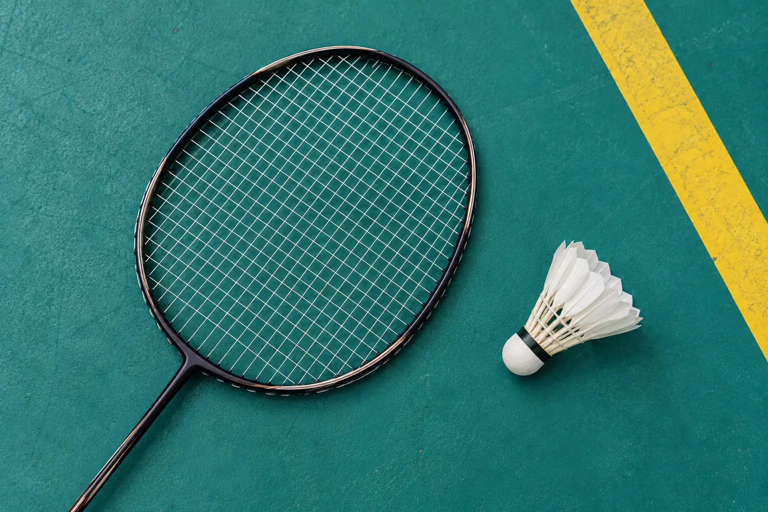 Illustration: The oval strung head of a plain badminton racket lies beside a white feather shuttlecock on teal flooring with one yellow sideline.
