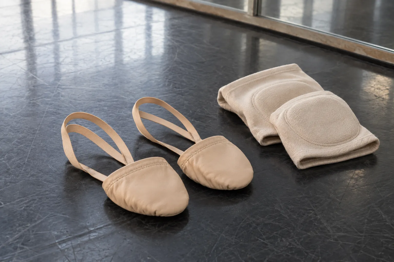 Illustration: Half-sole dance shoes and fabric knee pads on a rehearsal floor.
