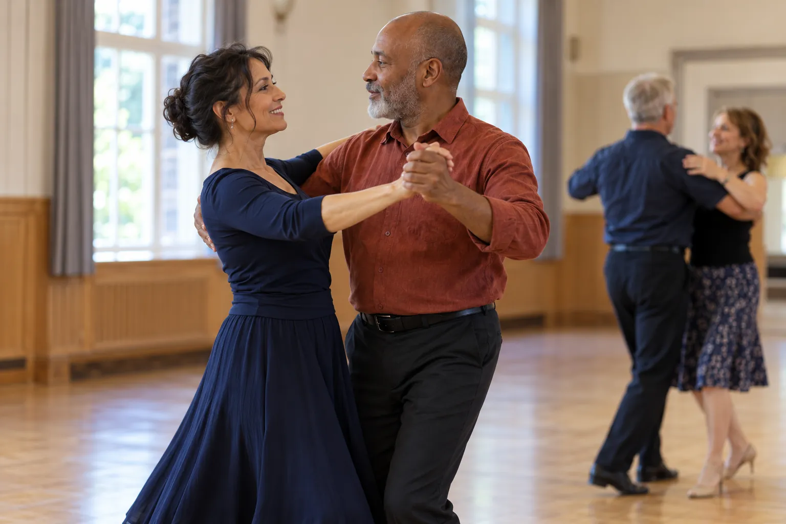 Illustration: Two adults rehearse a gentle ballroom step in a community hall while another pair practices farther back.