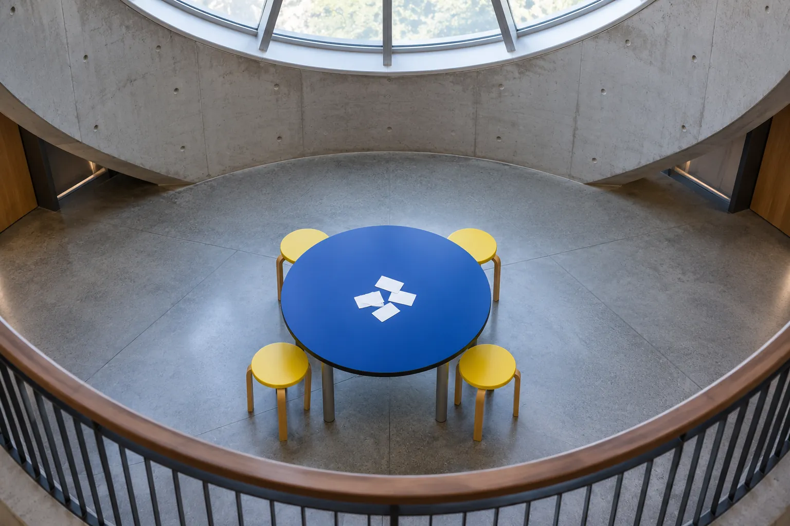 Illustration: A blue discussion table and yellow stools beneath a skylight.