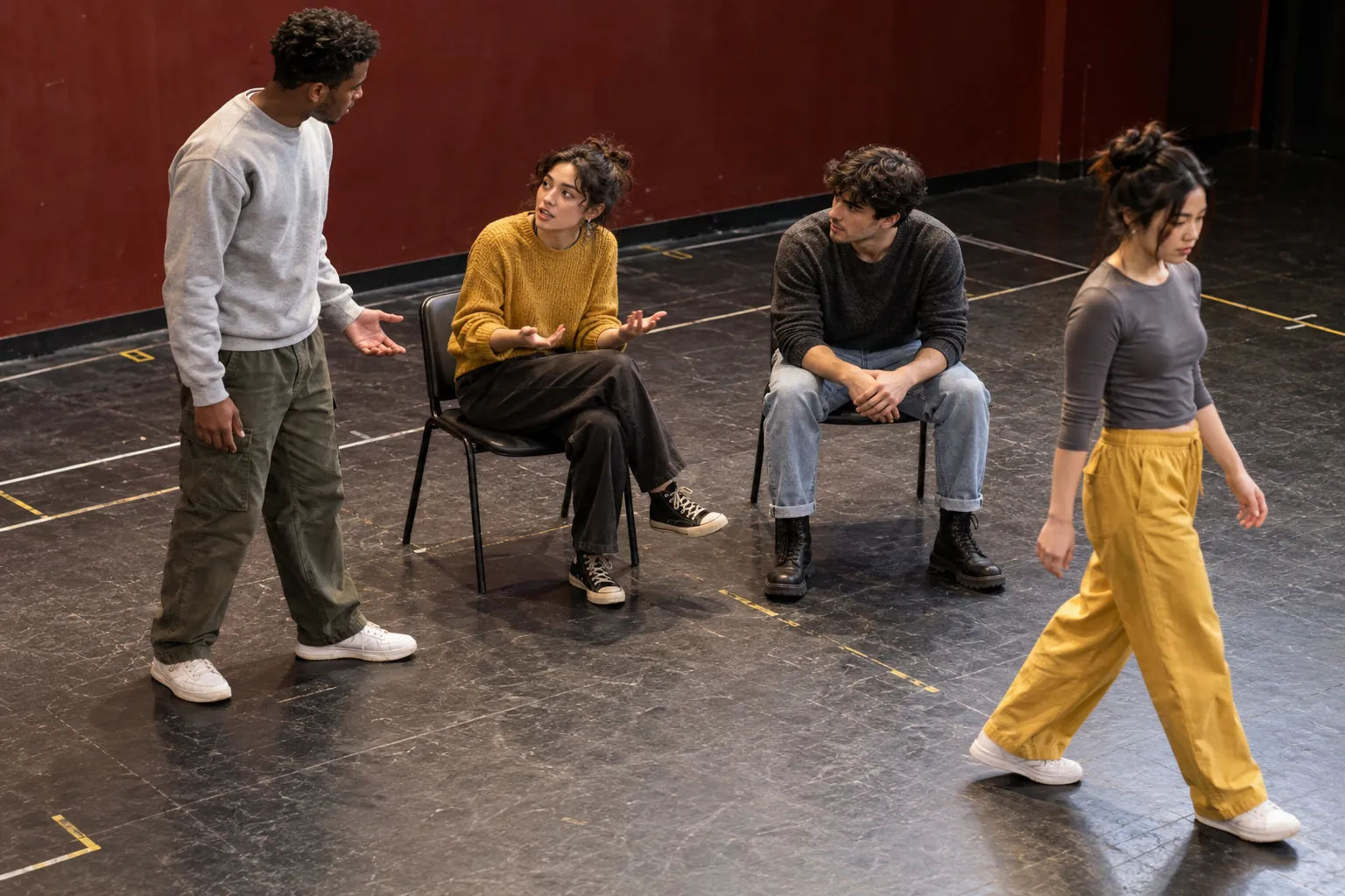 Illustration: Young adults rehearse a scene with chairs on a taped practice floor.