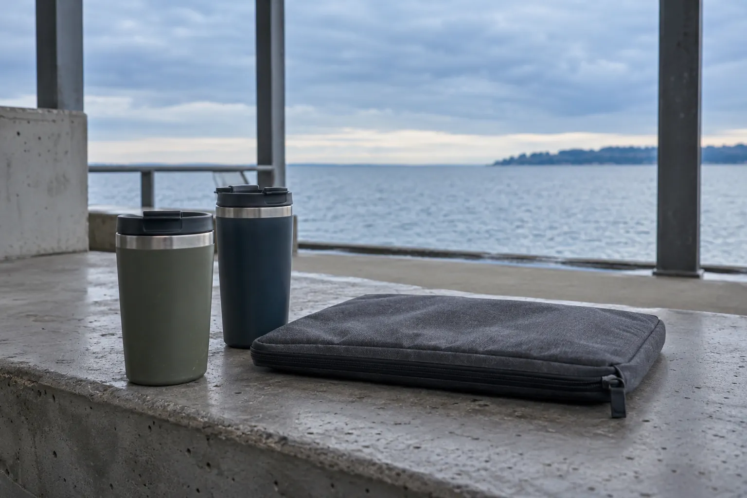 Illustration: Two reusable coffee tumblers and a plain document pouch occupy the broad concrete sill of an empty waterfront shelter.