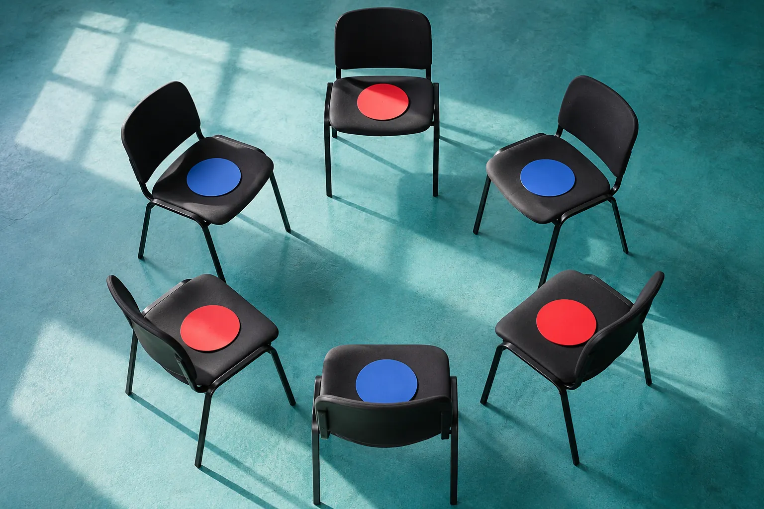 Illustration: Plain voting disks on chairs arranged in a turquoise-floored discussion circle.