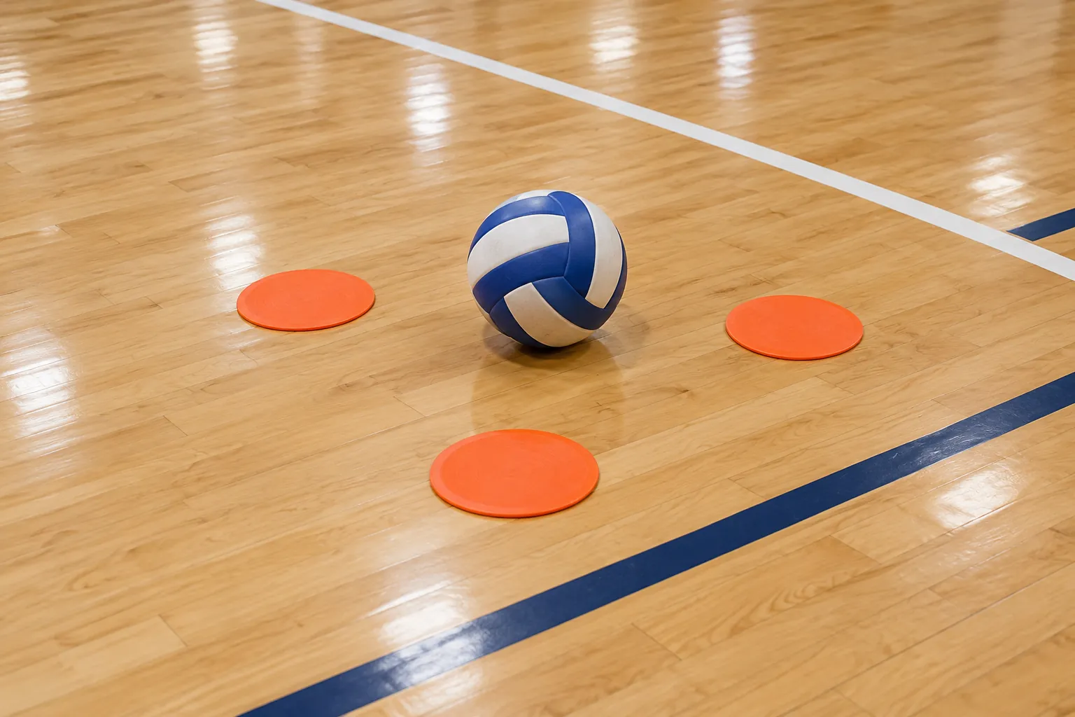 Illustration: A plain blue-and-white paneled volleyball and three flat orange target discs sit on an empty polished indoor court.